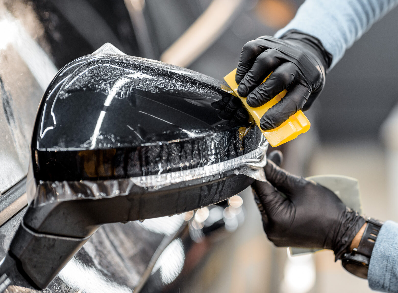 Man applying sticking protective film on a car mirror at the veh